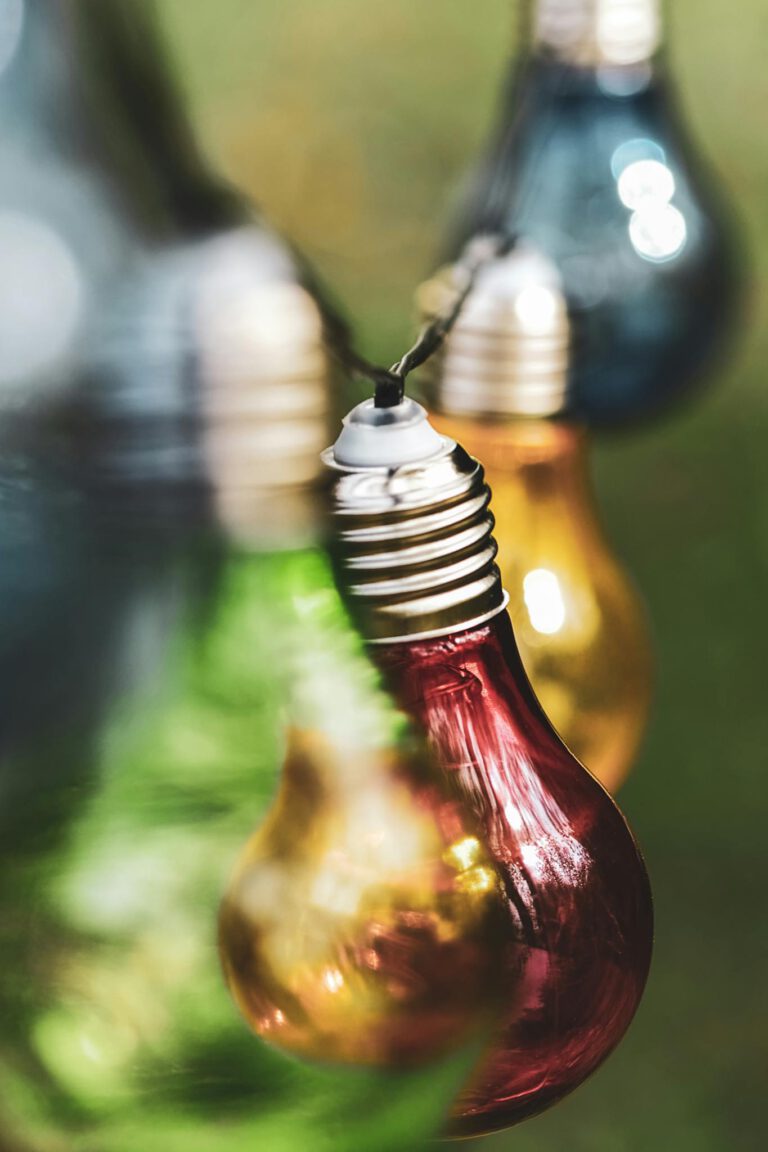 Close-up of vibrant colored light bulbs hanging outdoors with soft bokeh background.